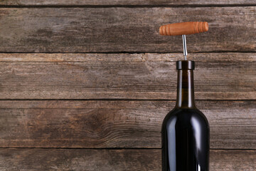 Wine bottle with corkscrew on wooden background, space for text