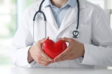 Doctor with red heart at white table in clinic, closeup