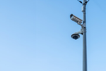 Security camera and dome camera on a pole with clear sky in the background