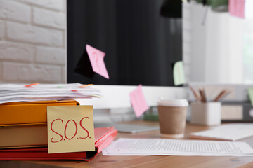 Note with word SOS and stationery on wooden table at workplace