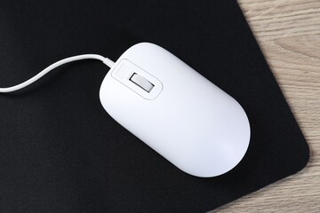 White computer mouse and black mousepad on wooden table, top view