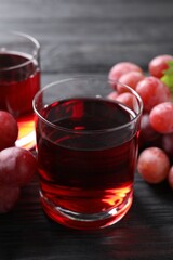 Tasty grape juice in glass and berries on black wooden table, closeup