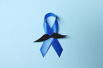 Blue ribbon and fake mustache on light background, top view. Prostate cancer awareness