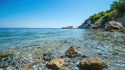 Crystal clear water covers pebbles on a greek island beach with a rocky cliff in the background