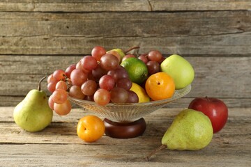 Glass vase with different fresh fruits on wooden table