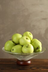 Glass vase with fresh green apples on wooden table against gray background, space for text