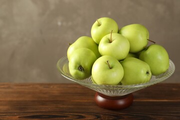 Glass vase with fresh green apples on wooden table against gray background, closeup. Space for text