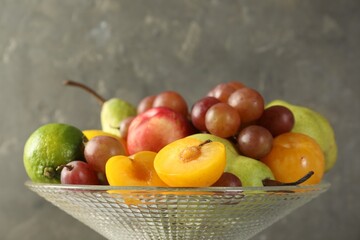 Glass vase with different fresh fruits on gray background, closeup