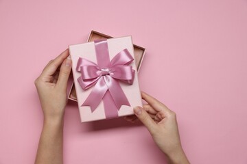 Woman decorating gift box with bow on pink background, top view