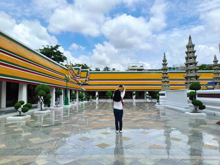 Obraz premium Asian woman take photo and travel in Wat Suthat Thepwararam temple beautiful temple architecture. Bangkok’s tourist attractions. Tourist backpack travel in buddhist temple take photo with smartphone