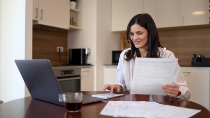 Beautiful woman using laptop and calculating her finances at home