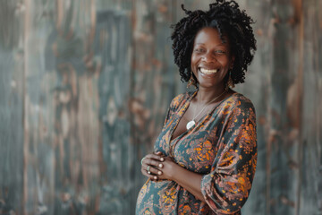 Joyful pregnant woman with curly hair smiling warmly, standing against a textured wall.