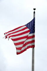 A tattered red white and blue American flag blowing in the wind atop of a flagpole. 