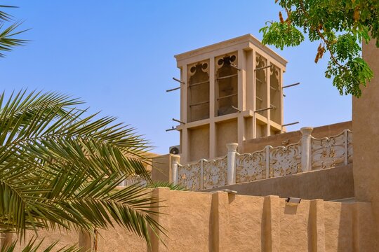 Traditional Arabic house with wind catcher tower or Barjeel for cross ventilation and passive cooling in building. Facade with palm tree, arch windows and typical middle eastern geometric ornament. 