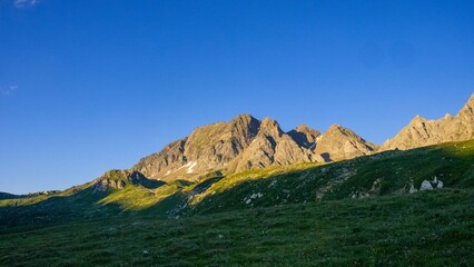 Lush green meadow with rocky peaks against blue sky in the background on a sunny day in Riale, Italy