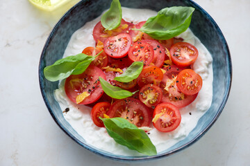 Stracciatella or stretched curd cheese served with fresh tomatoes and green basil in a blue bowl, horizontal shot, middle close-up