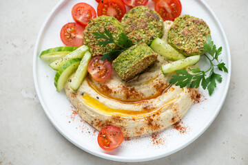 Hummus with paprika, falafel, fresh tomatoes and cucumber served on a white plate, middle close-up, horizontal shot