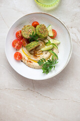 Plate with hummus, falafel and fresh vegetables, vertical shot on a beige stone background with space, flat lay
