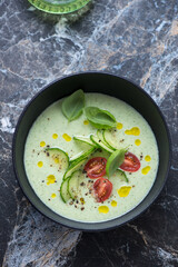 Bowl of chilled cucumber and green basil soup, vertical shot on a black marble background, high angle view