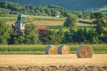 Ländliche Gegend mit Streuobstwiesen, Strohballen vor Maisfeld vor historischen Gebäude mit...