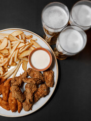 Delicious snacks with juicy chicken strips on crispy French fries, accompanied by a beautiful glass of beer in a cozy nice restaurant