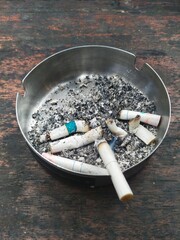various used cigarette filters in a stainless ashtray on a wooden table
