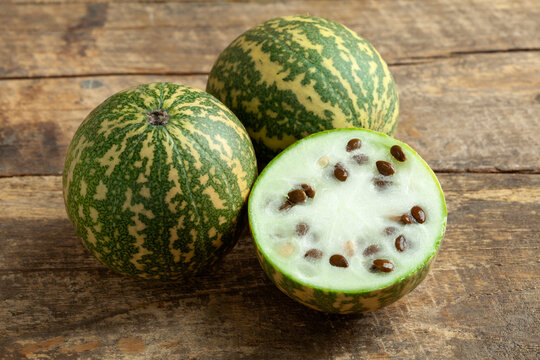 Whole and halved small red seeded citron melon on wooden background close up