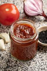Glass jar with Tomato Onion chutney and nigella seeds close up for a side dish 