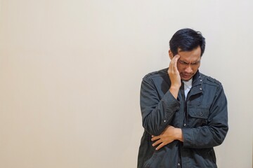 A Southeast Asian man wear brown jacket, put hand on forehead forehead, suffer from headache isolated on cream background. People lifestyle concept, Suffering migraine.
