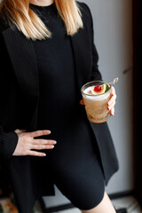 sweet girl in a beautiful black dress holds a cool refreshing cocktail in her hands in a cozy nice restaurant