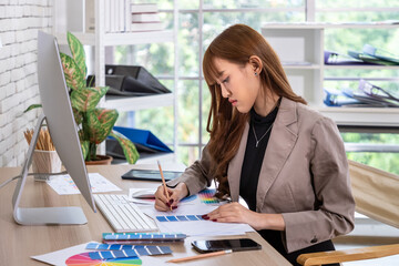 Asian female woman dedicated graphic designer working with color palettes and sketches in modern office environment