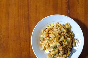 Stir fried spicy macaroni on white platree with fork, in the wood table, homemade food.