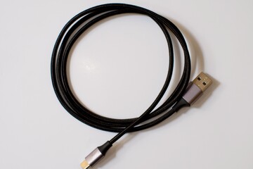 A blackUSB type C charger cable, compatible for many devices, wrapped in a spiral shape, isolated on white background.