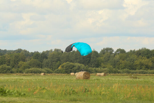 The parachutist landed in a field behind a roll of hay. The parachute canopy hovered above the ground.