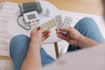 Close-up of elderly man sitting sofa at living room measures blood pressure with device. Senior...