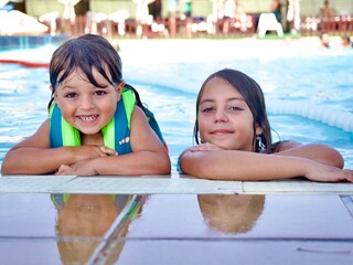“Close-up portrait of two smiling Caucasian siblings at the pool”