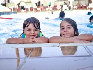Retrato de cerca de dos niños pequeños disfrutando de un baño, descansando al borde de la piscina en un día soleado.
