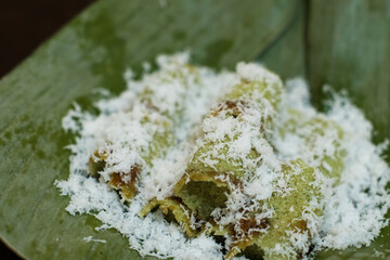 Kue putu in a plate covered with banana leaves in brown background, is a type of traditional Indonesian snack filled with palm sugar, wrapped with grated coconut, and rice flour.