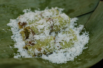 Kue putu in a plate covered with banana leaves in brown background, is a type of traditional Indonesian snack filled with palm sugar, wrapped with grated coconut, and rice flour.