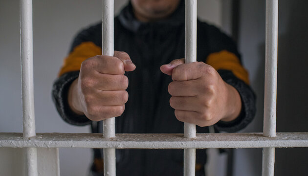 檻に閉じ込められた男性の手　鉄格子を掴む刑務所の犯罪者　Hands of prisoner holding bars in jail