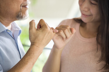 Senior man hooking little finger for pinky promise with middle aged daughter, concept image for...