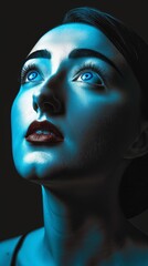 A woman's face is illuminated by a blue light, creating a dramatic and ethereal effect. Her eyes are wide open, and her lips are slightly parted.