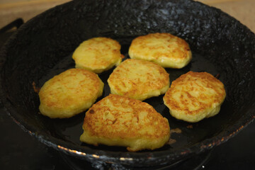 Close-up of golden homemade zucchini fritters sizzling in a frying pan on a stovetop