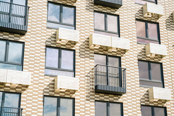 Modern apartment building facade with alternating balconies and large windows reflecting the sky.