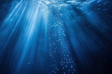 Obraz premium Abstract underwater background with bubbles and light rays in dark blue water, closeup view.