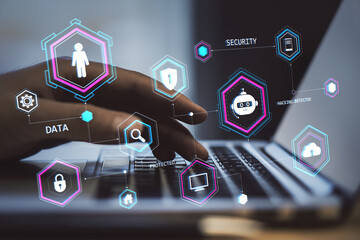 Hand typing on laptop keyboard with holographic security and data icons overlayed.