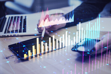 Person analyzing financial graphs on digital tablet and laptop in office setting.