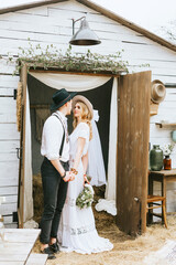 wedding boho style ceremony young couple newlyweds bride in white dress with veil and groom in hat and jeans with suspenders hugging and having fun at barn of country house, shot in motion