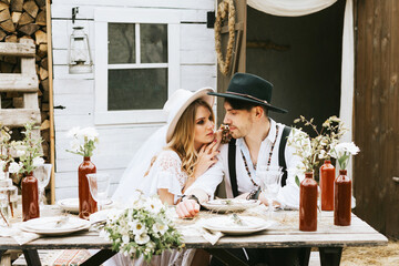 wedding boho style ceremony young couple newlyweds bride in white dress with veil and groom in hat and jeans with suspenders hugging and having fun at barn of country house, shot in motion