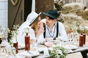 wedding boho style ceremony young couple newlyweds bride in white dress with veil and groom in hat and jeans with suspenders hugging and having fun at barn of country house, shot in motion